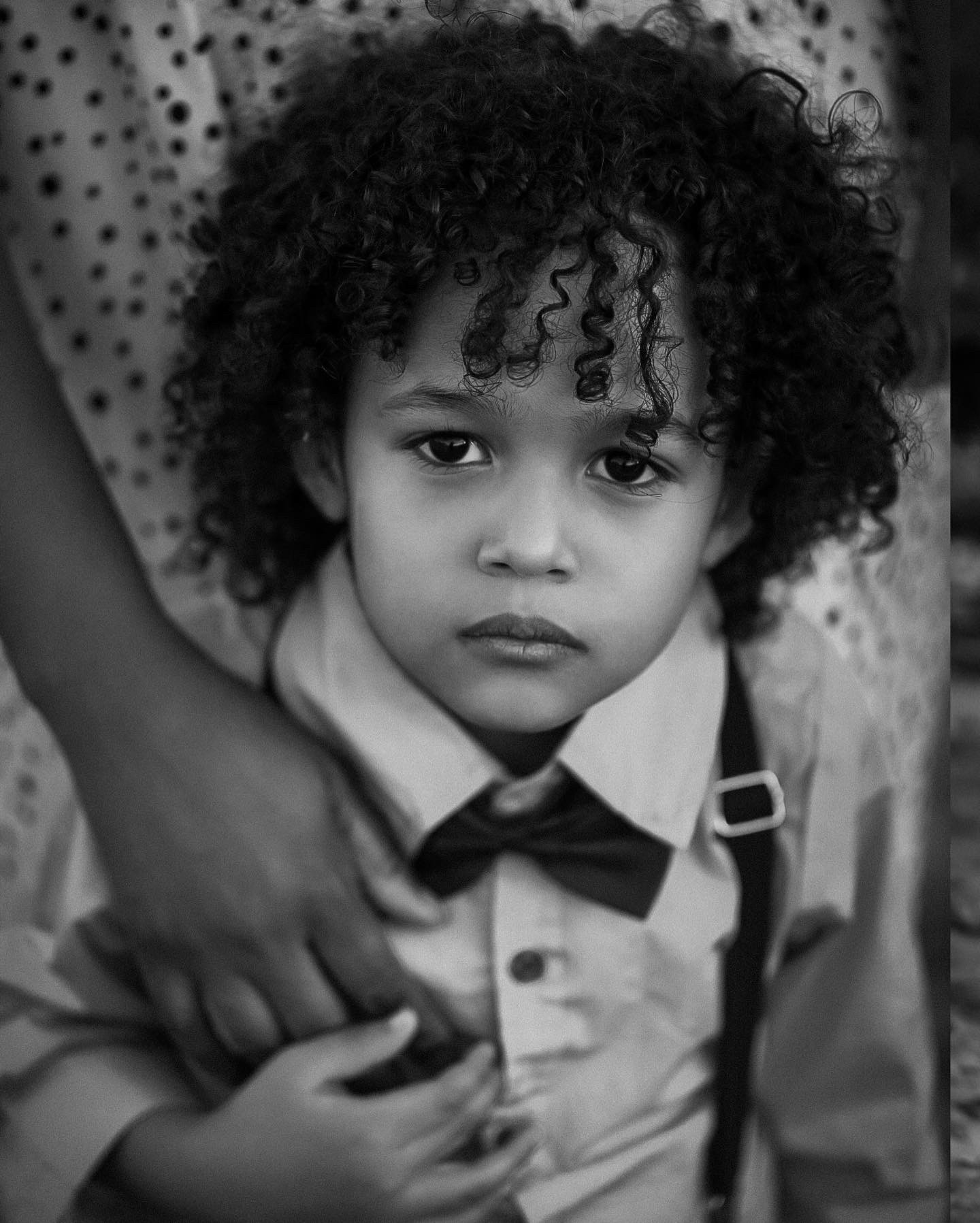 Black and white portrait of a young son holding his moms arm and looking at the camera with a serious face