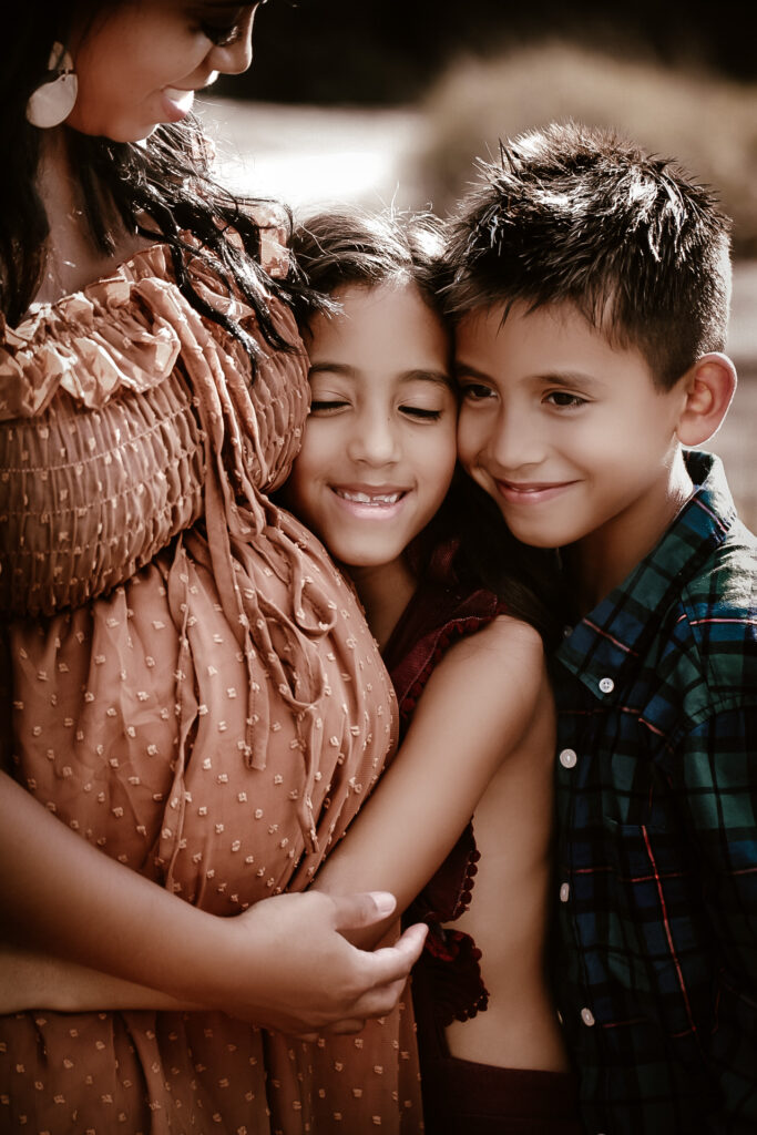 Young daughter and son hugging their pregnant mom's belly and smiling