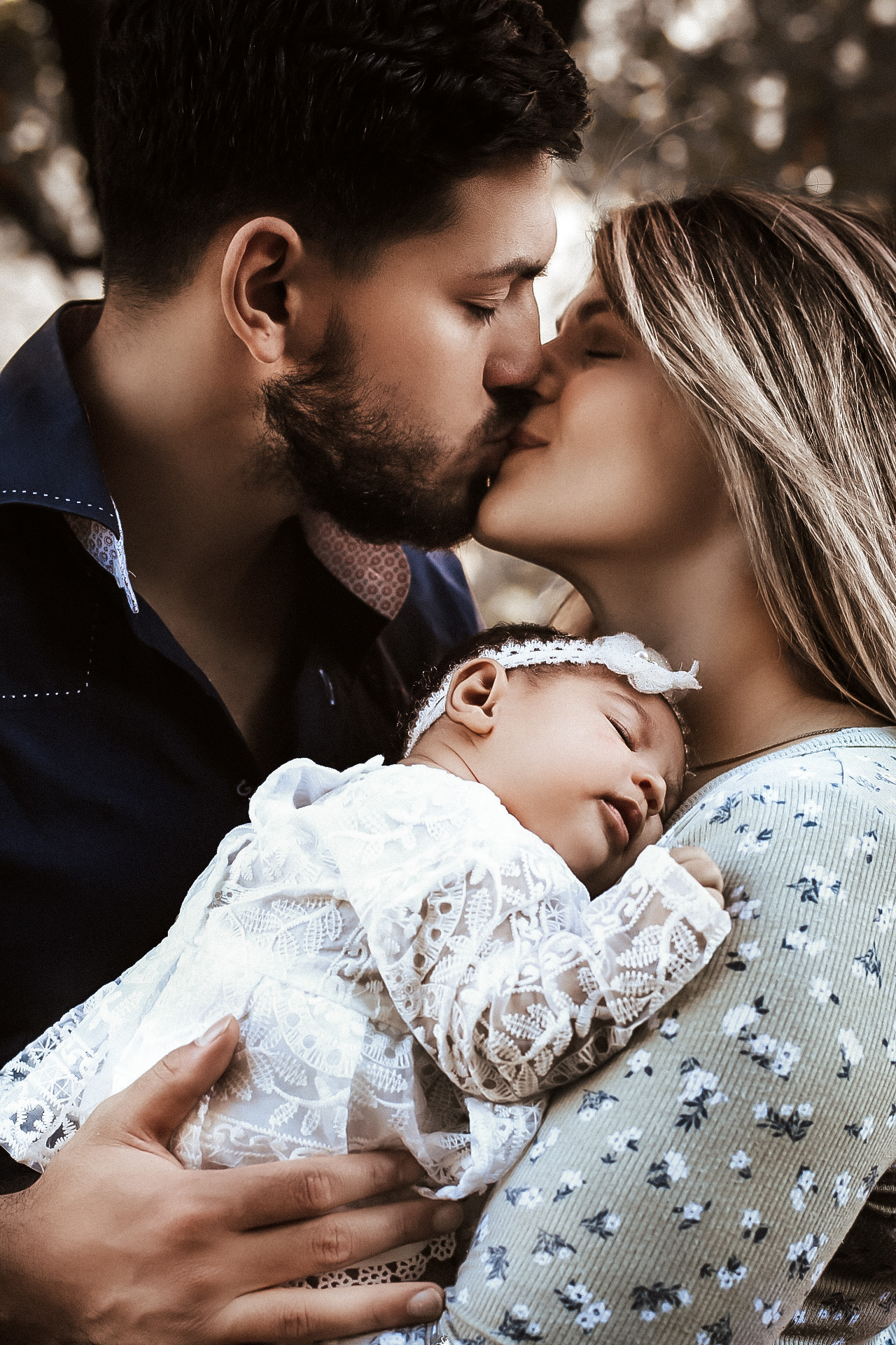 Husband and wife kissing each other while holding a newborn baby.