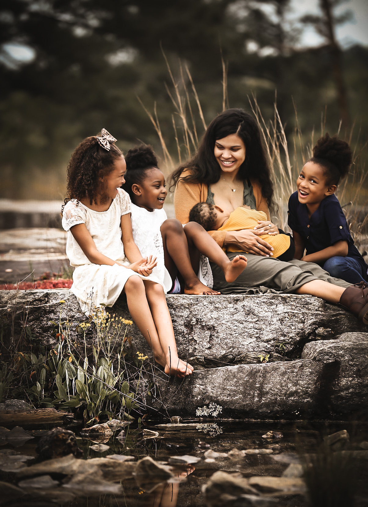 Family of 5 sitting on a rock at Arabia Mountain in Atlanta, GA while all looking at each other and smiling and mom holding a little baby