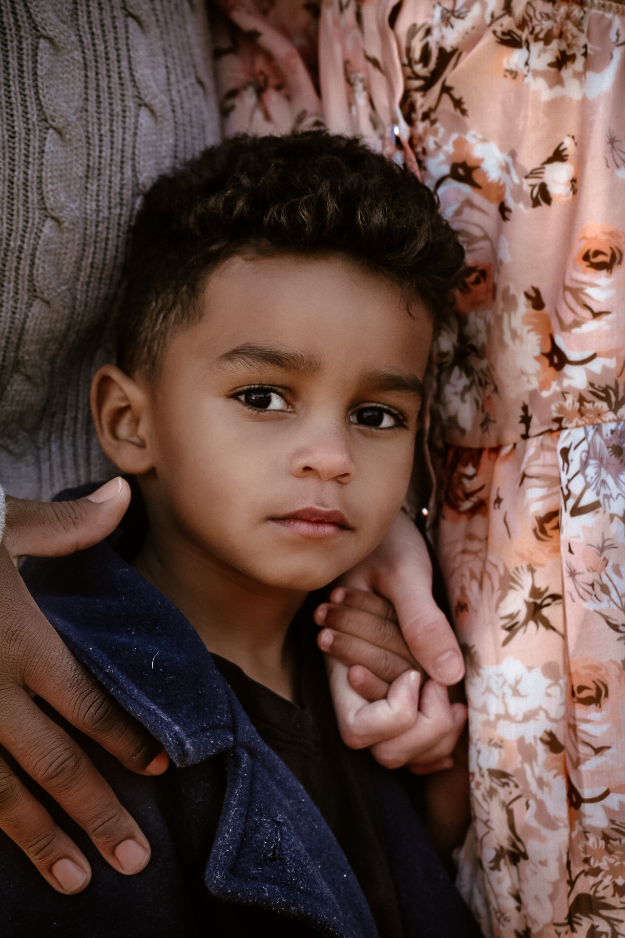 CLose up of young son standing closely to his mom and dad while looking at the camera with a serious dace