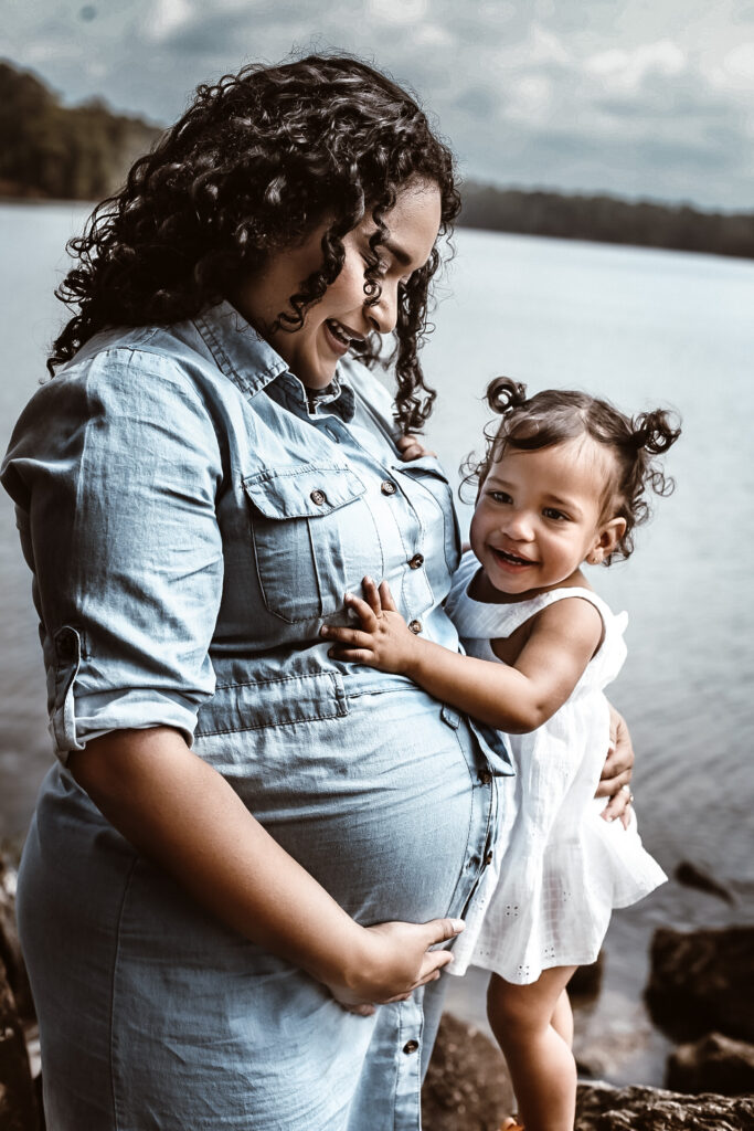 Young daughter hugging pregnant mom while mom is looking at her belly