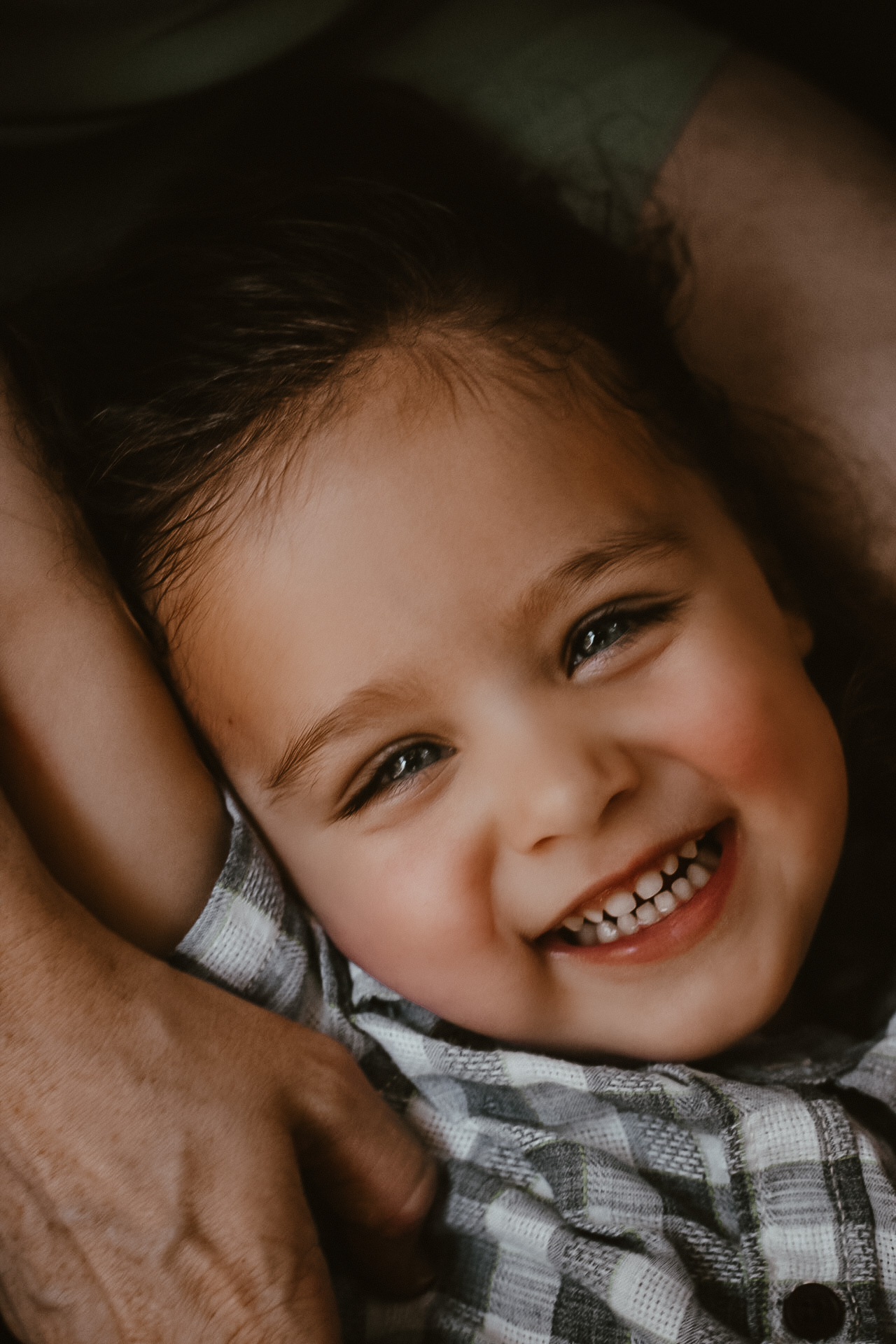 Little boy laying on his moms lap while smiling at the camera