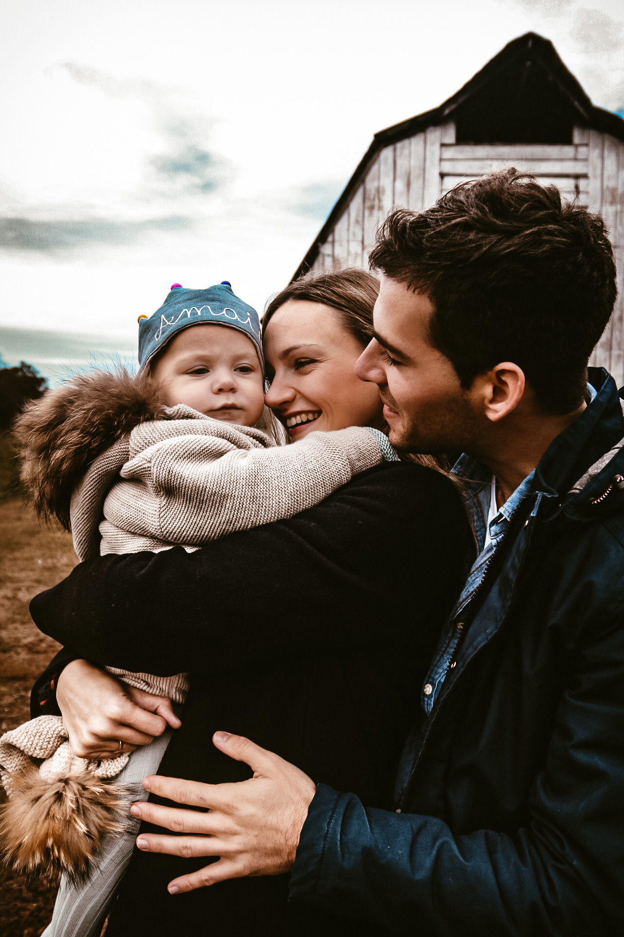 Mom and dad holding their young baby boy at a barn in Atlanta, Ga, while closely hugging and looking at him and smiling