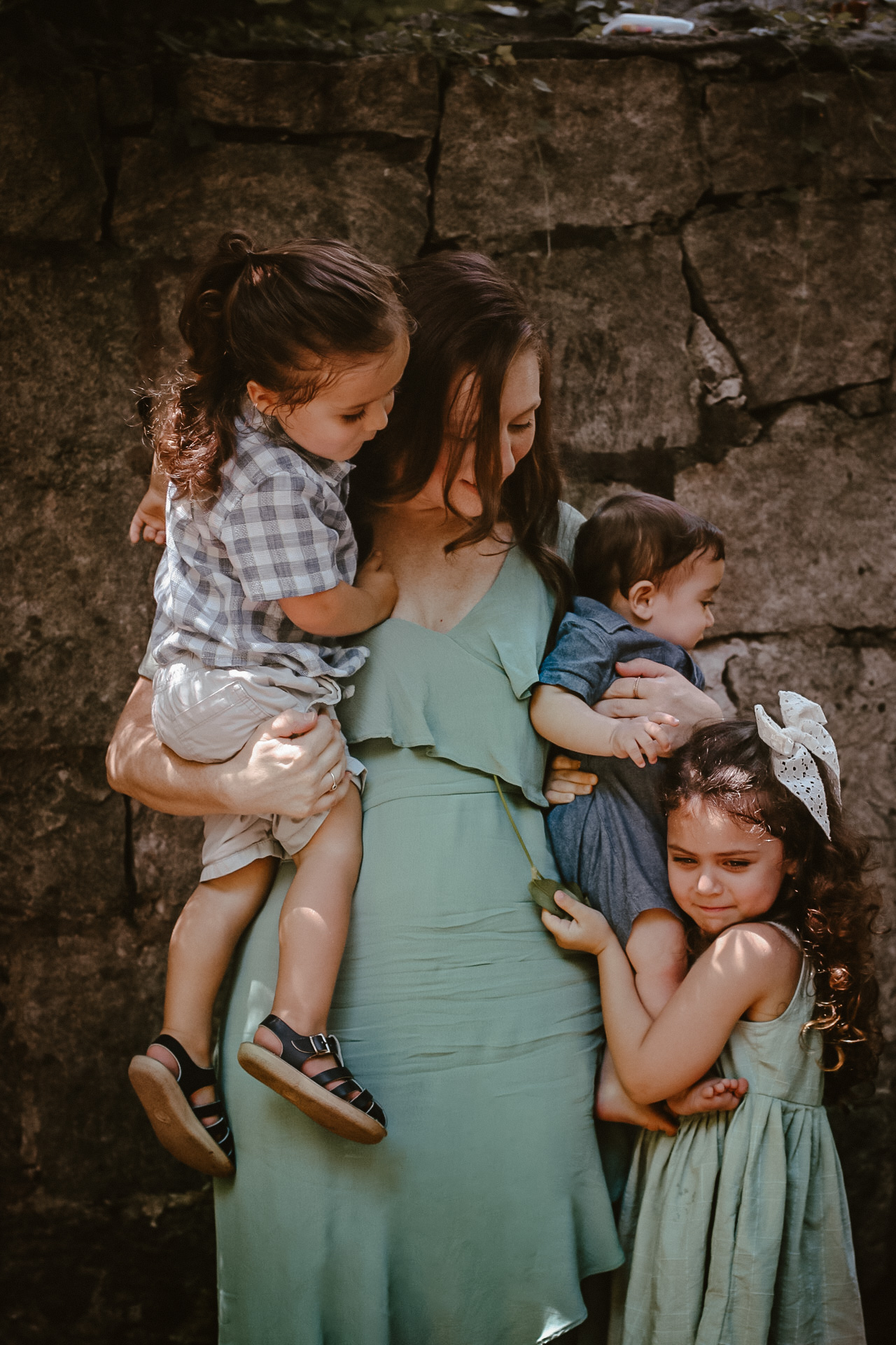 Mom holding her three baby while looking down at daughter and smiling