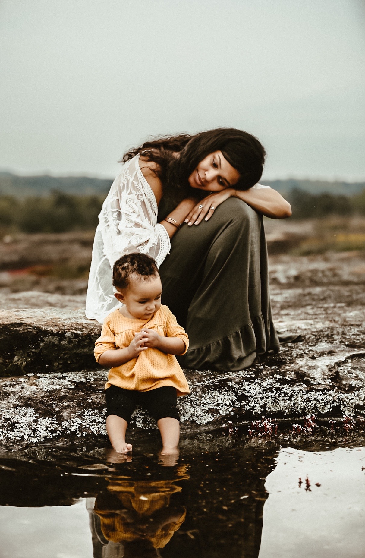 mom and little baby sitting on top of Arabia Mountain in Atlanta, Ga while baby is sitting near a small pond and mom and laying on her knees gazing at her