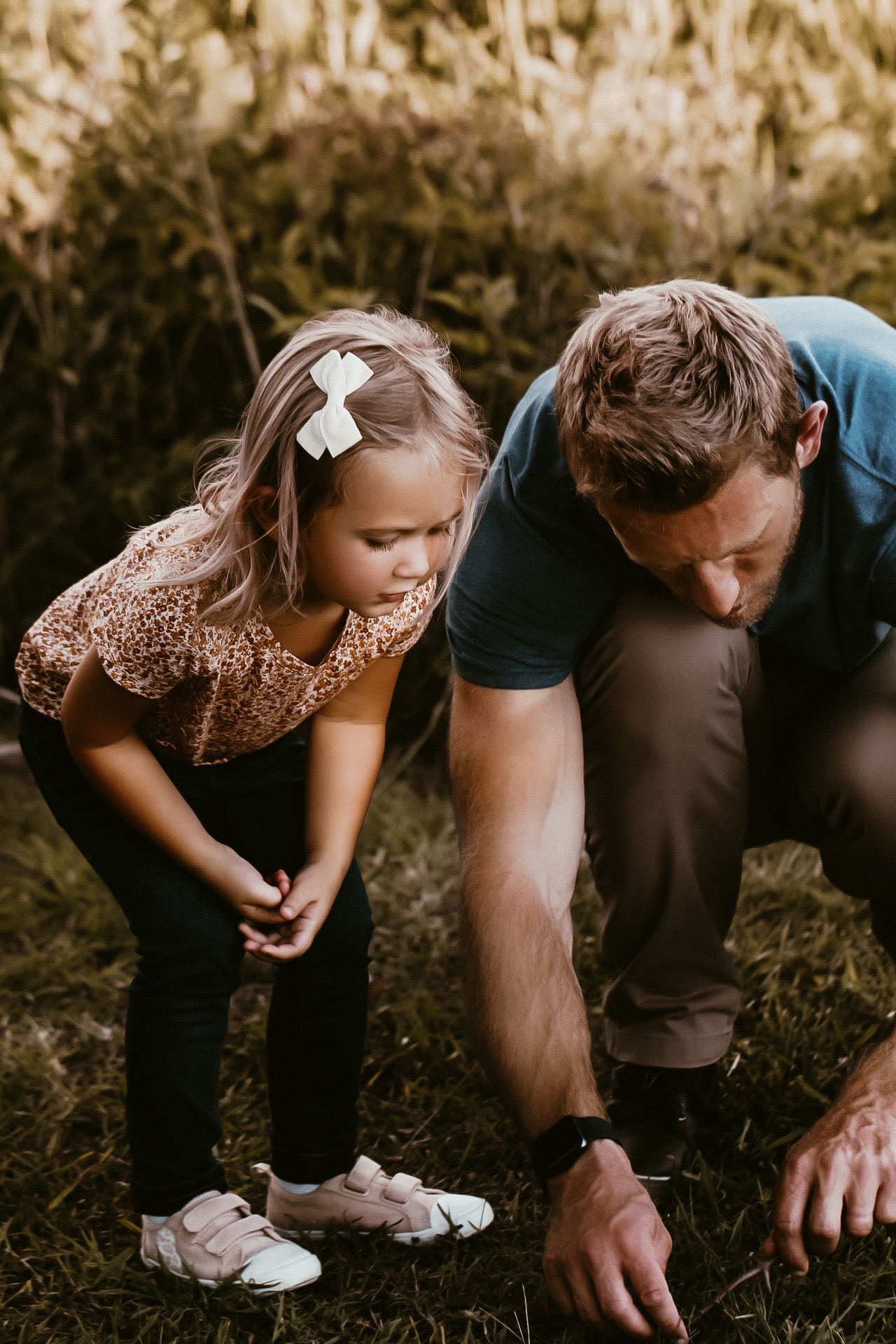 Father and his daughter kneeling down at the ground looking at an insect. Location Acworth Beach in Atlanta Ga