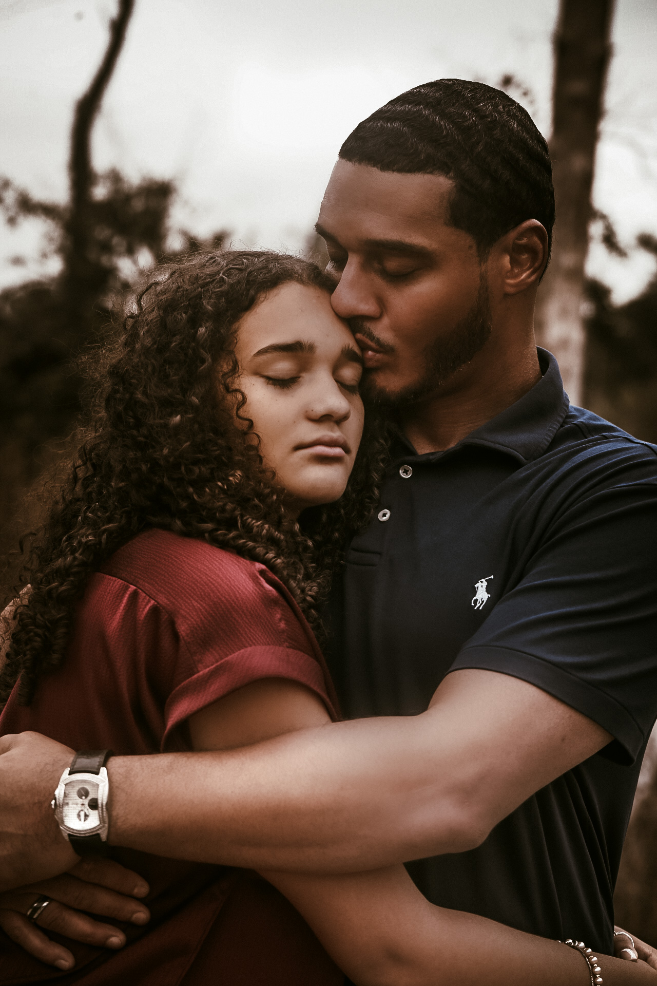 Dad and daughter hugging while dad is kissing her on the forehead with their eyes closed