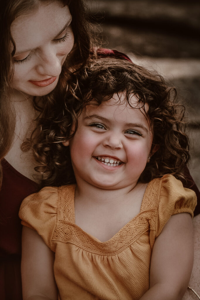 Little girl sitting in he rmom's lap while smiling at the camera