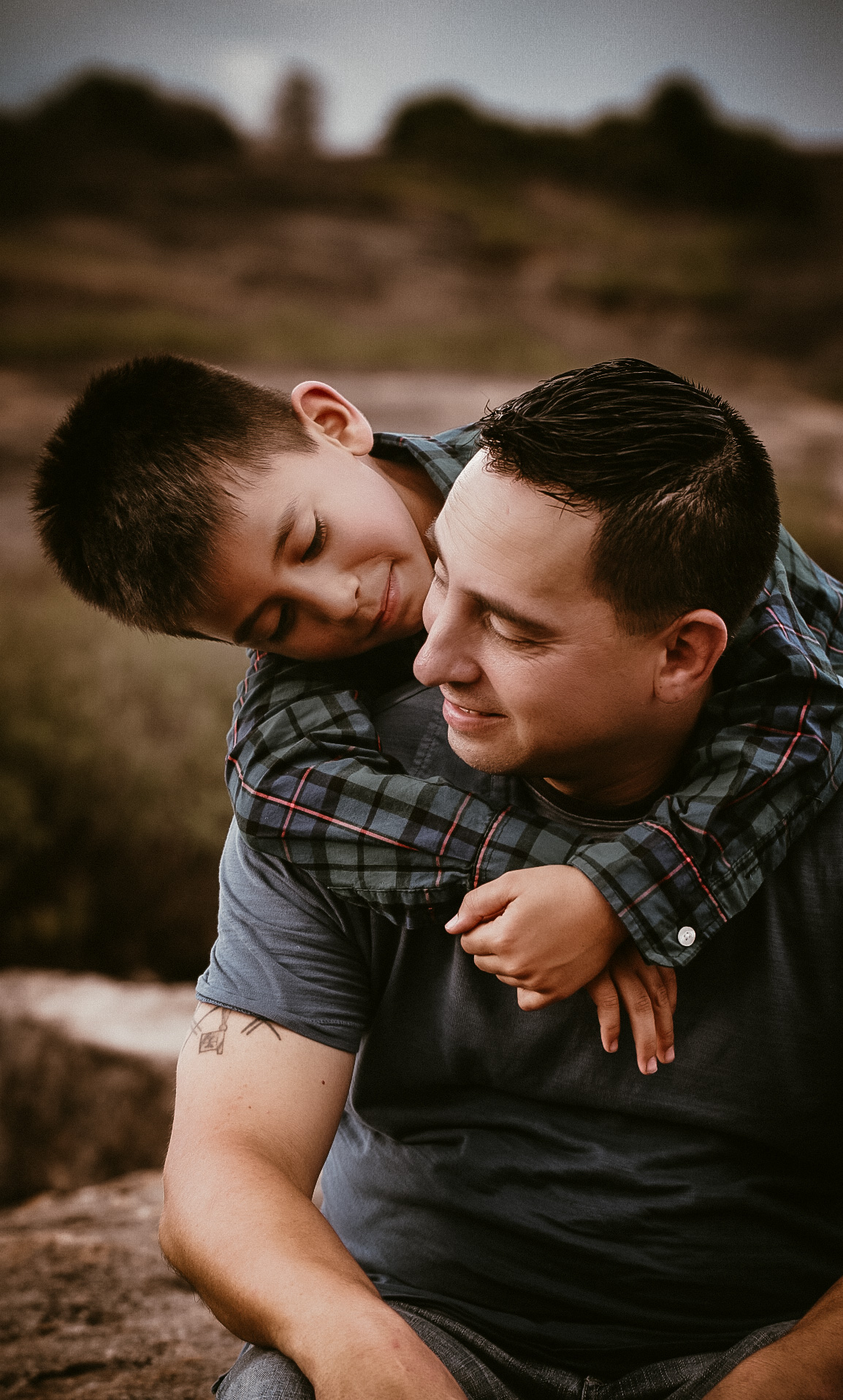 Son hugging his dad from behind while they are both looking at each other and smiling