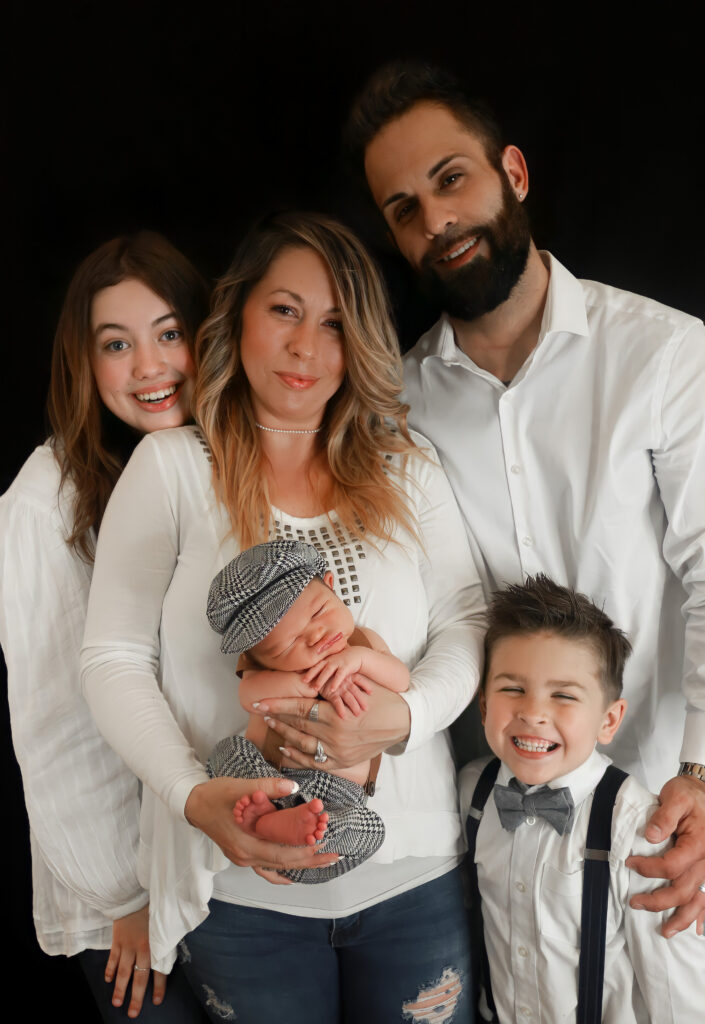 Studio portrait of a family of 5 mom holding a newborn baby and all smiling at the camera