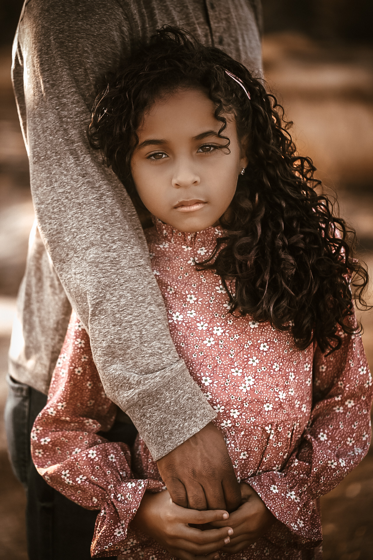 Little girl holding her dad's arm while gazing at the camera with a serious face