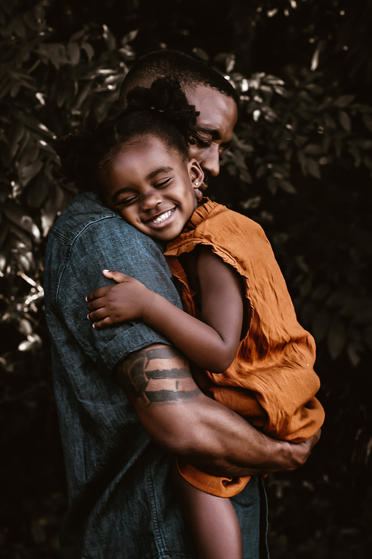 Dad holding his young daughter while she is laying his should and smiling with her eyes closed