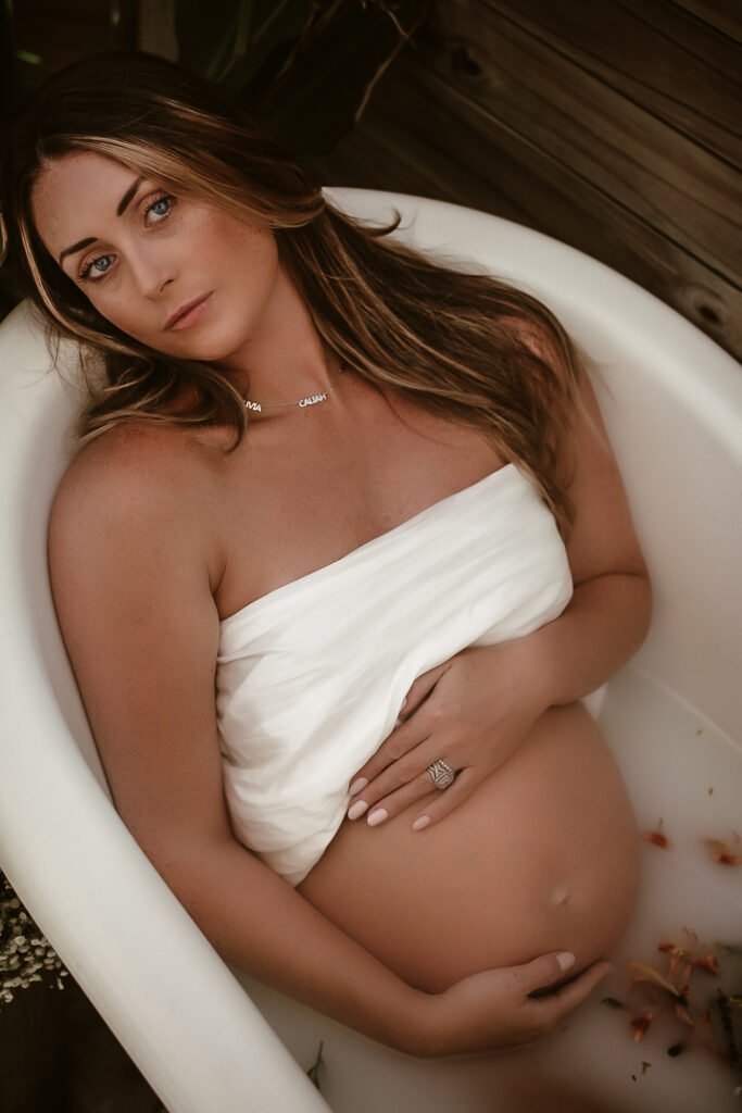 Pregnant mom in a bathtub holding her belly and looking at the camera