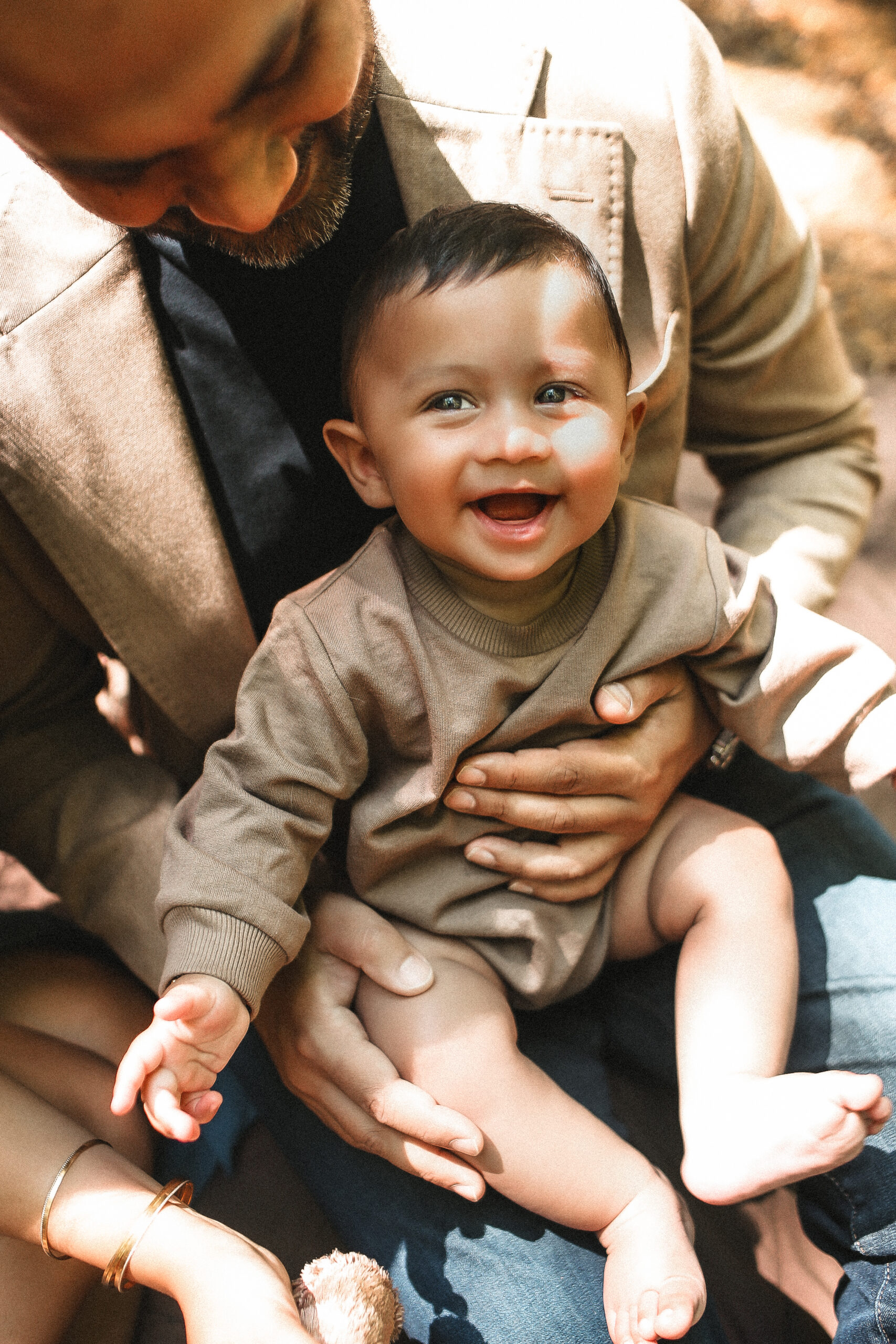 Little baby sitting in his dad's lap while laughing at the camera. Fall Family photography - portrait- Green Meadow Preserve Family photography