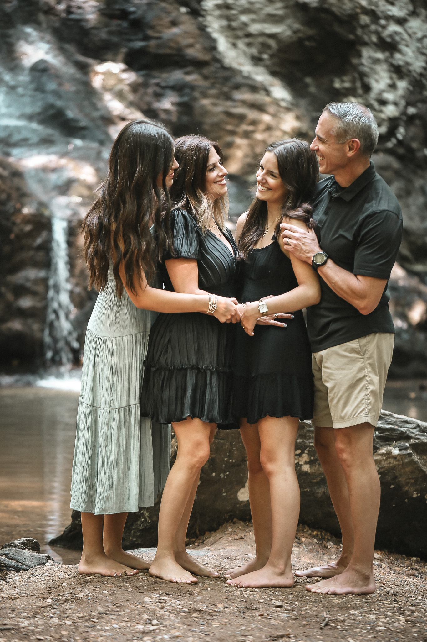 Two teen daughters hugging mom and dad as they look at eachother. High Shoals Falls family photography in Georgia