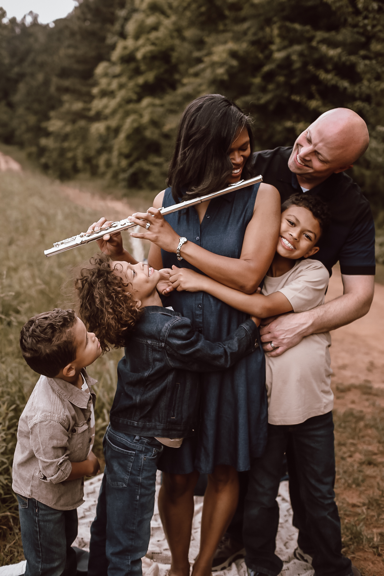 Family of 5 hugging each other and smiling at mom as she is holding a flute and looking at her son. Fall Family photography - portrait- Green Meadow Preserve Family photo