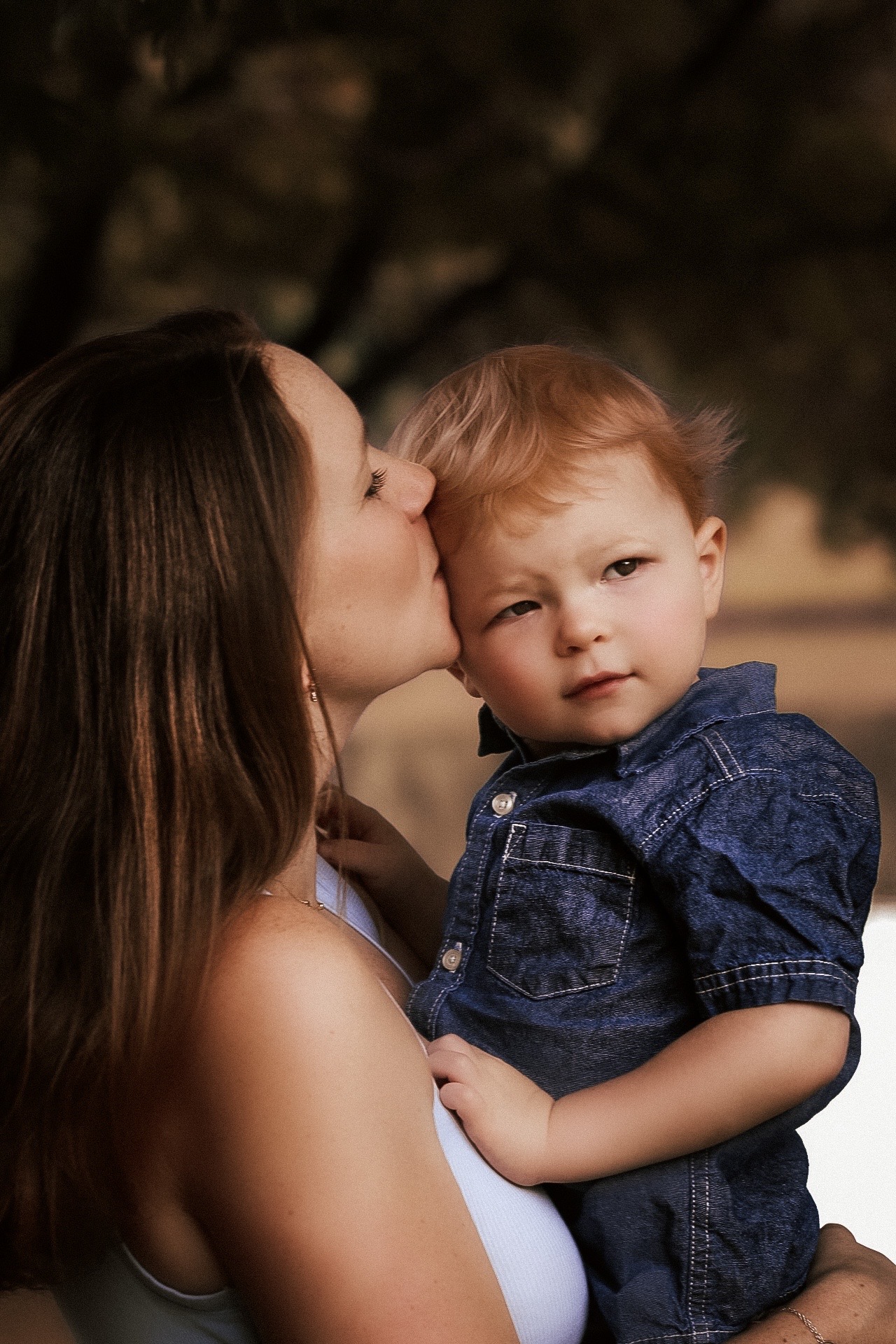 Mom holding her son and kissing him on the cheeck as he looks off into the distance - Motherhood Portrait- Atlanta Georgia