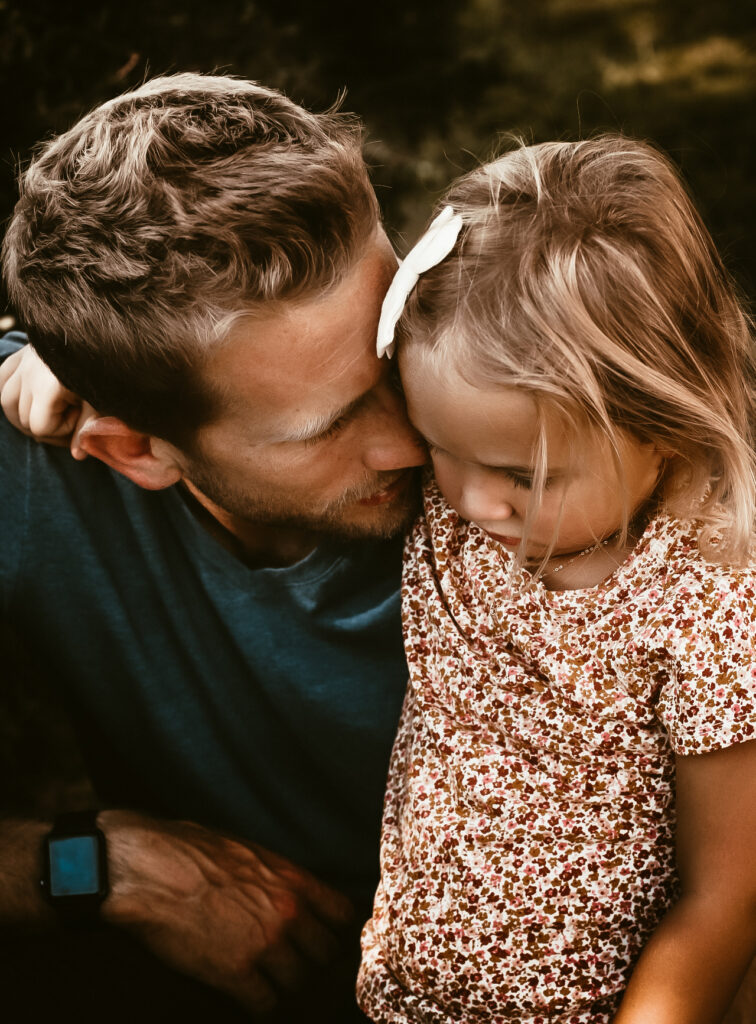 Dad holding his young daughter closely while telling her a secret and embracing each other