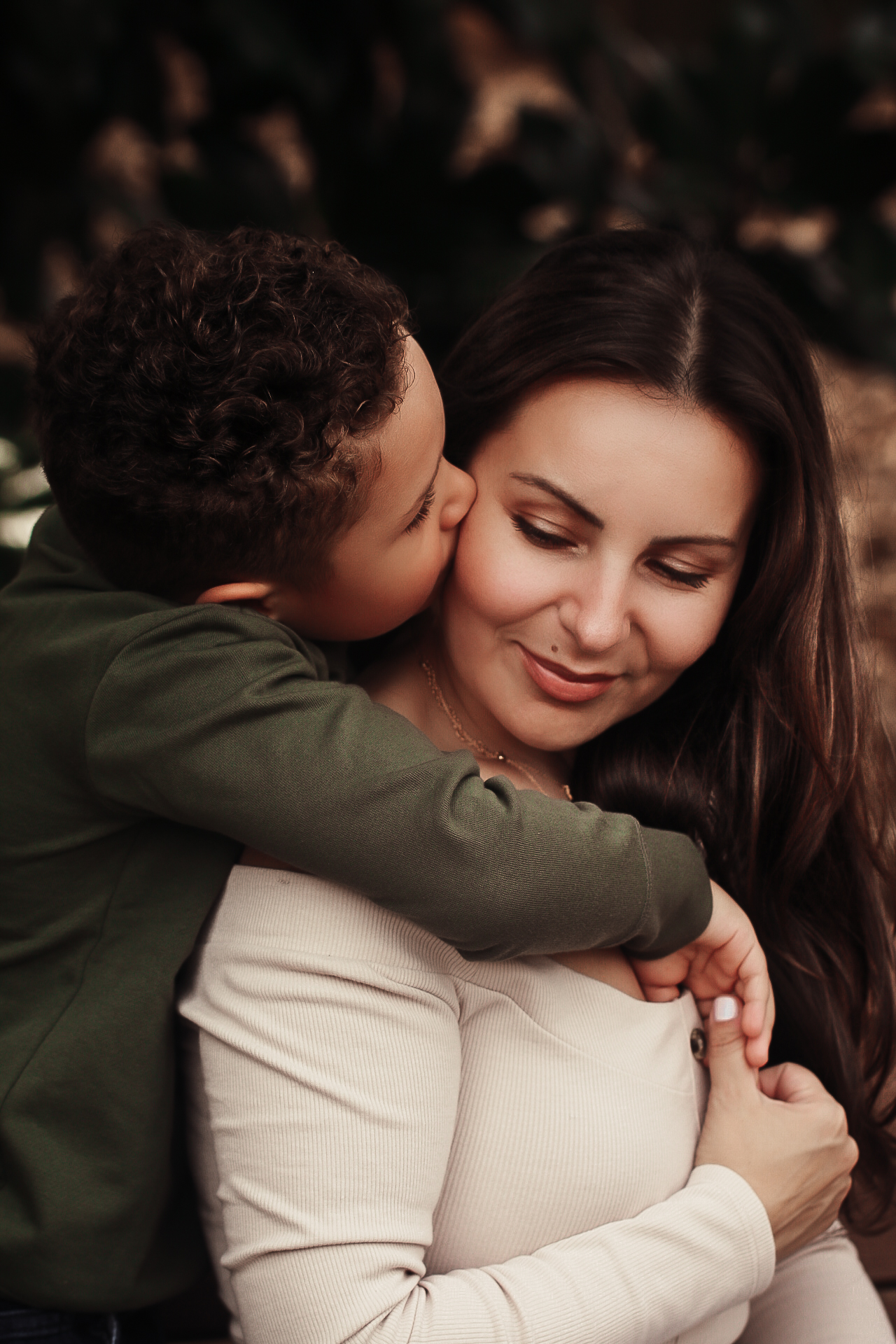 Son hugging his mom from behind and kissing her on the cheek while both have their eyes closed. Mother-son family photography in Georgia