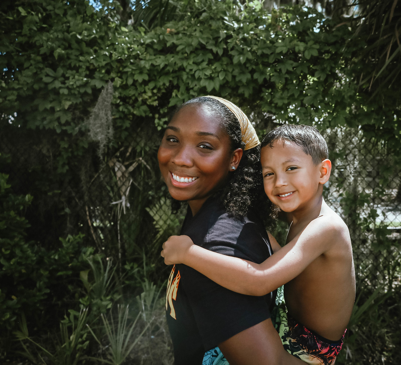 A photo of Ashley, owner of Ashley Aria Photography, at Woodlands Camp in Cleveland, Ga , giving a piggy back ride to a young boy while both smiling at the camera.