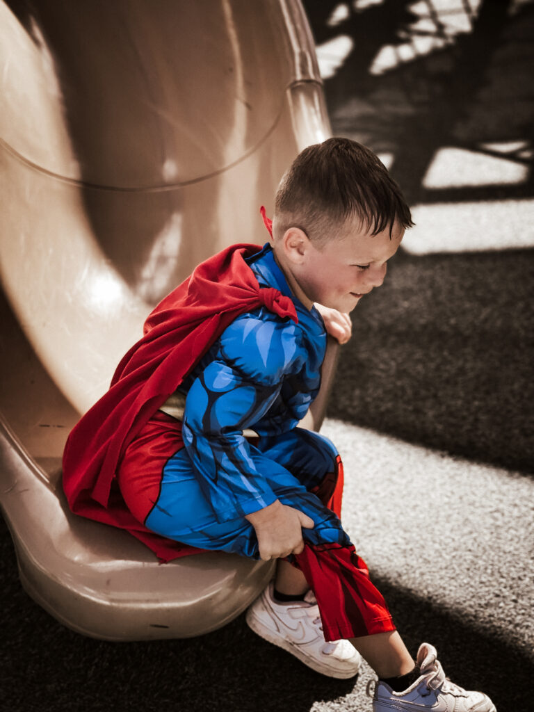 Little boy in a superman costume going down the slide at swift cantrell park