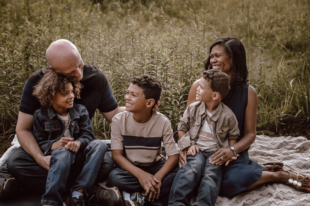 A family of 5 sitting in the grass in a big field located in Atlanta Ga, while looking at each other and laughing