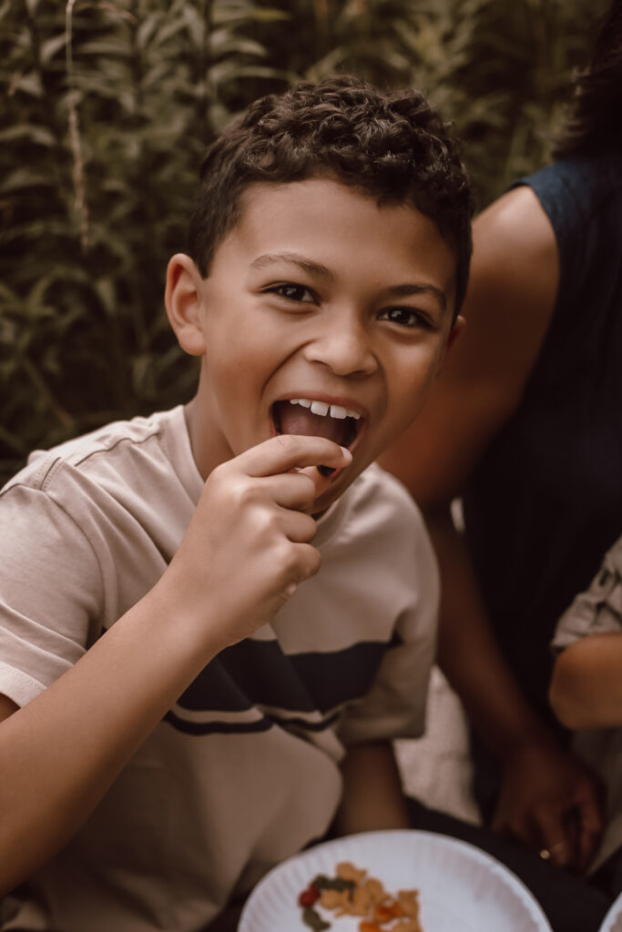 A young boy in a big field in Atlanta Ga, smiling at the camera while holding a blueberry