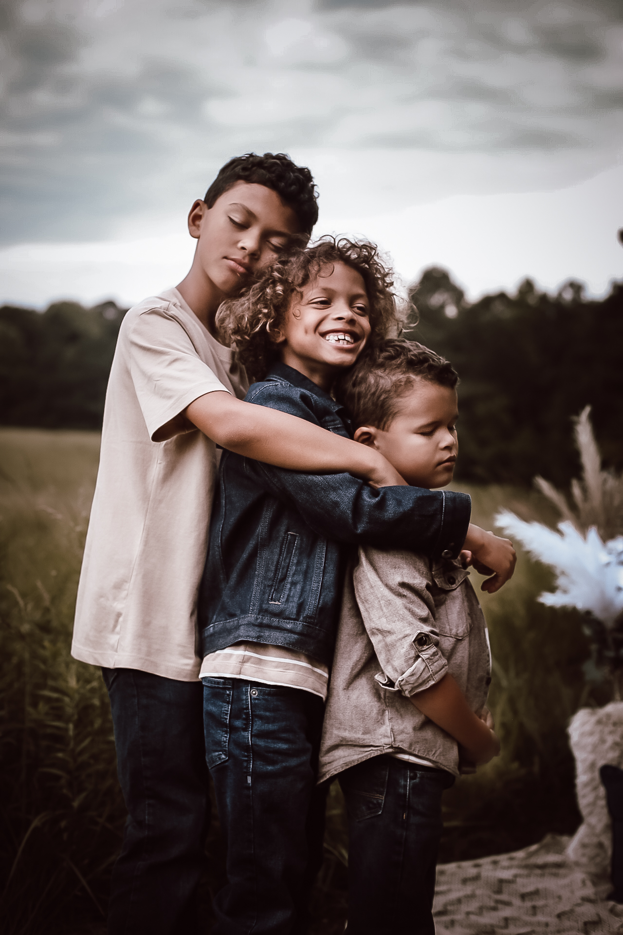 Three brothers hugging each other in a line with their eyes closed, in a big open field