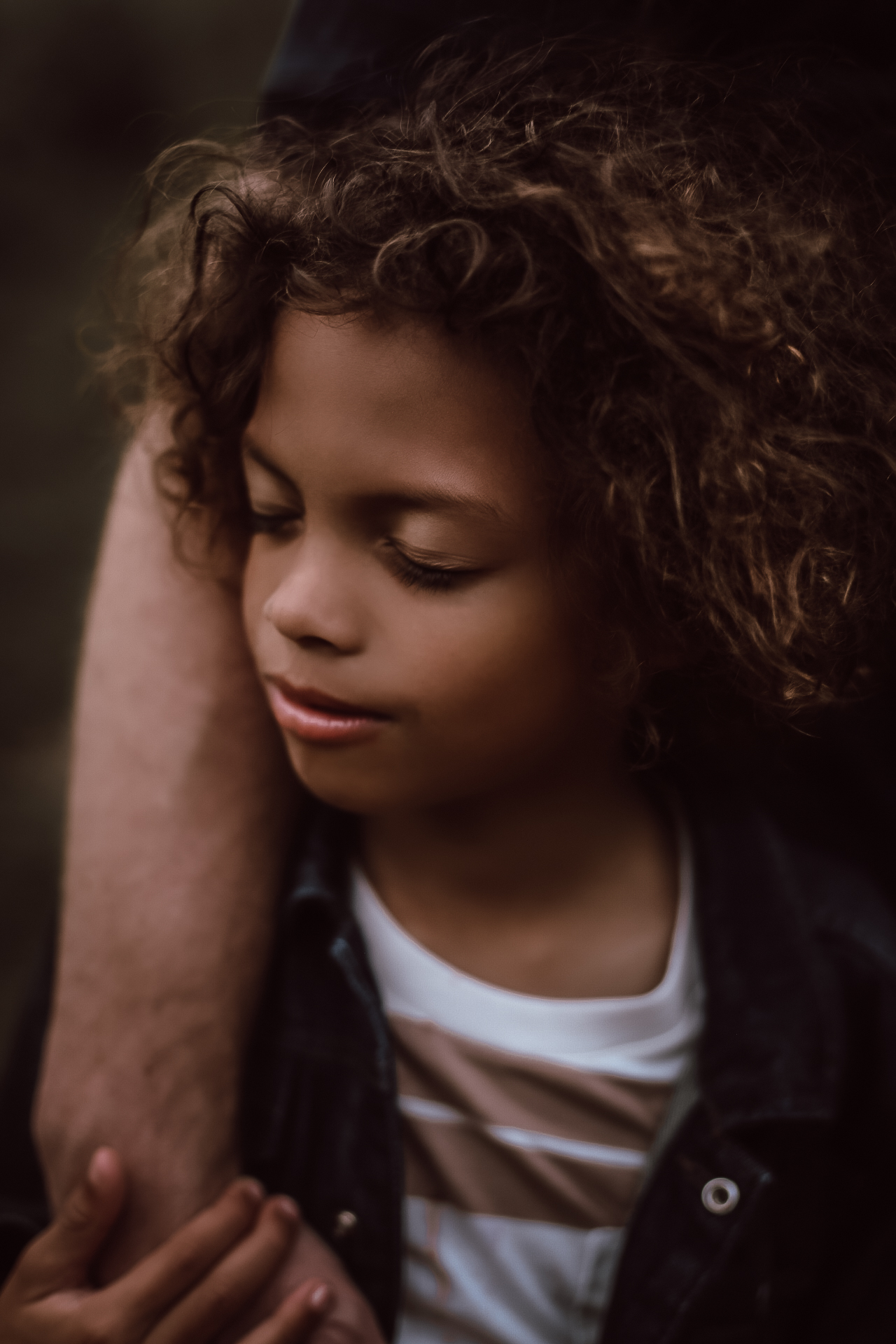 A young boy hold his dad's arm with his eyes closed, located in a big field in Atlanta, Ga