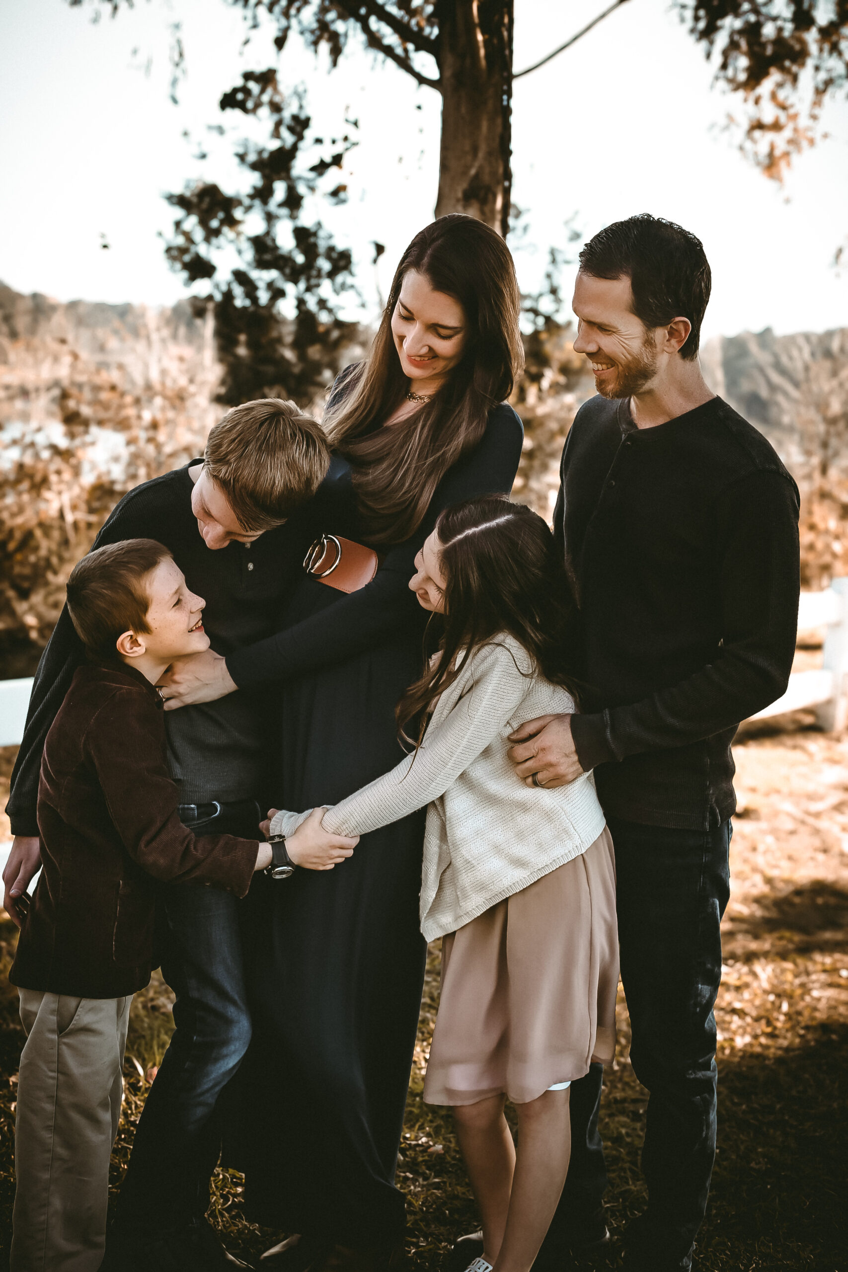 Family of 5 hugging and looking at eachother and smiling at eachother