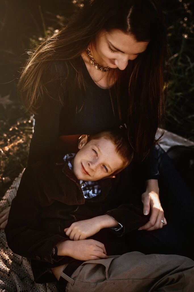 Little boy laying on his moms lap and looking at the camera with a soft smile