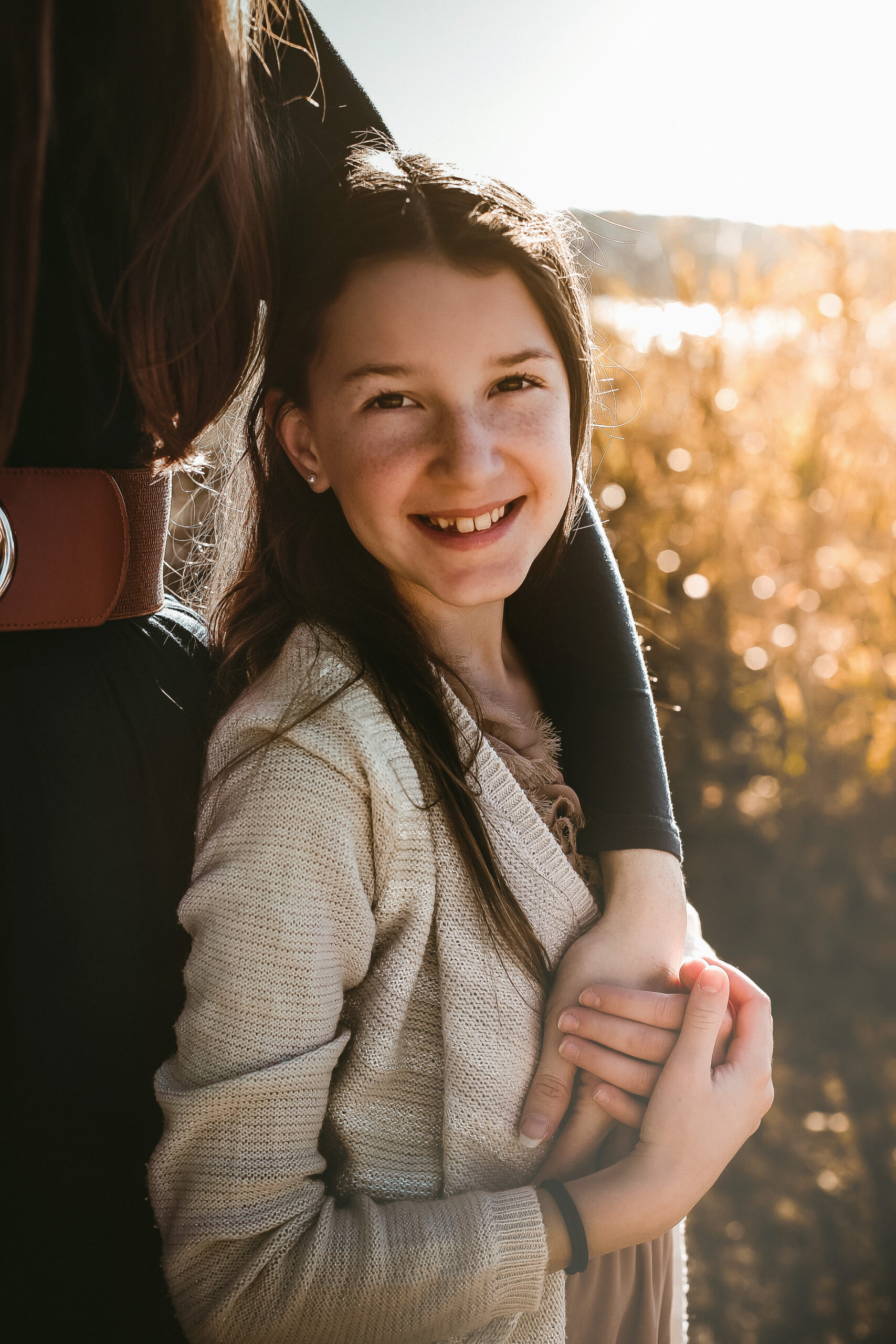 Little girl holding her moms arm and smiling at the camera