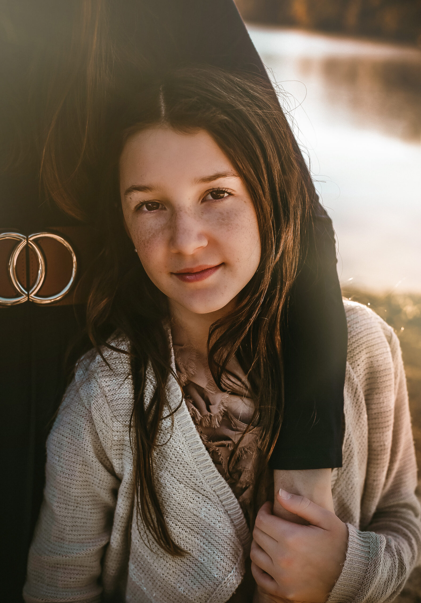 Little girl gazing into the camera at sunset while holding her moms arm