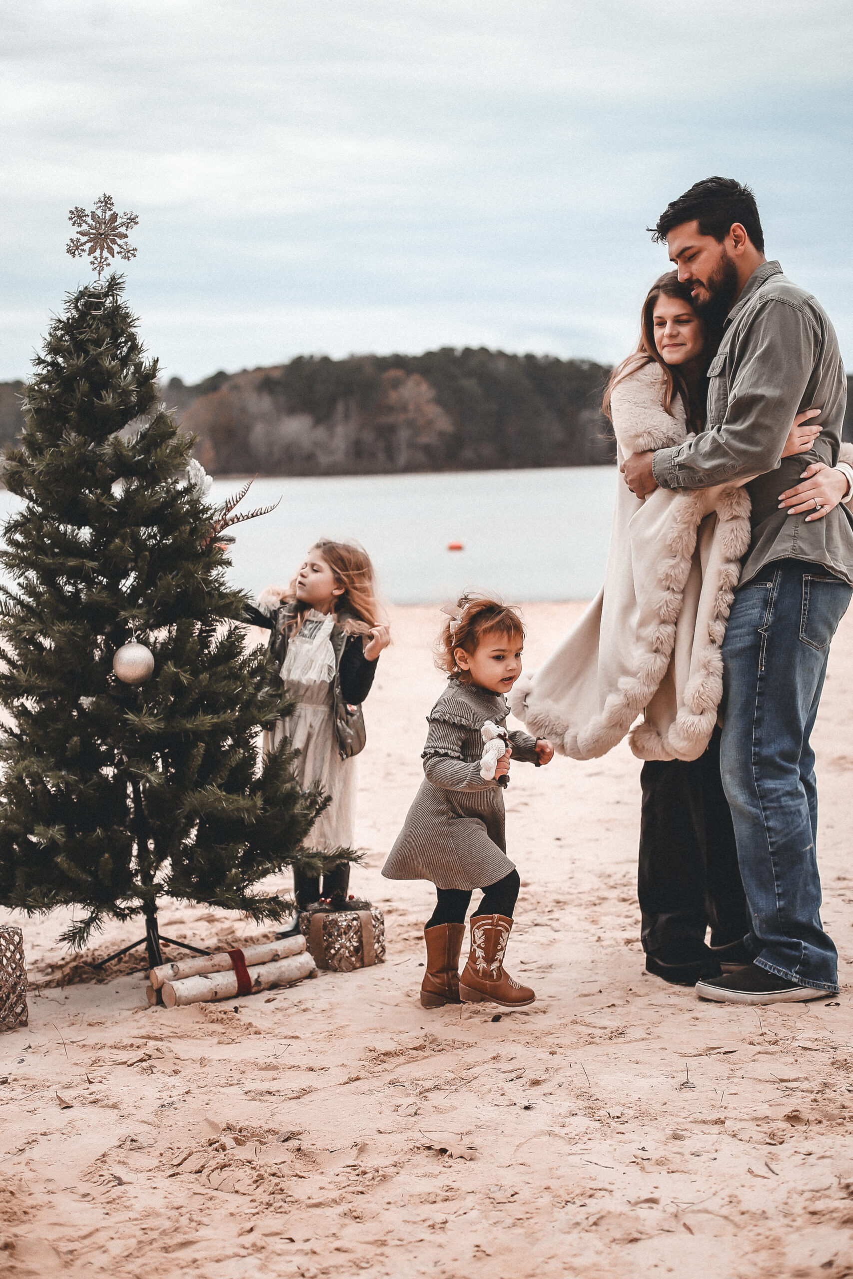 Family of 4 standing on the sand with two little girls putting ornaments on the cristmas tree