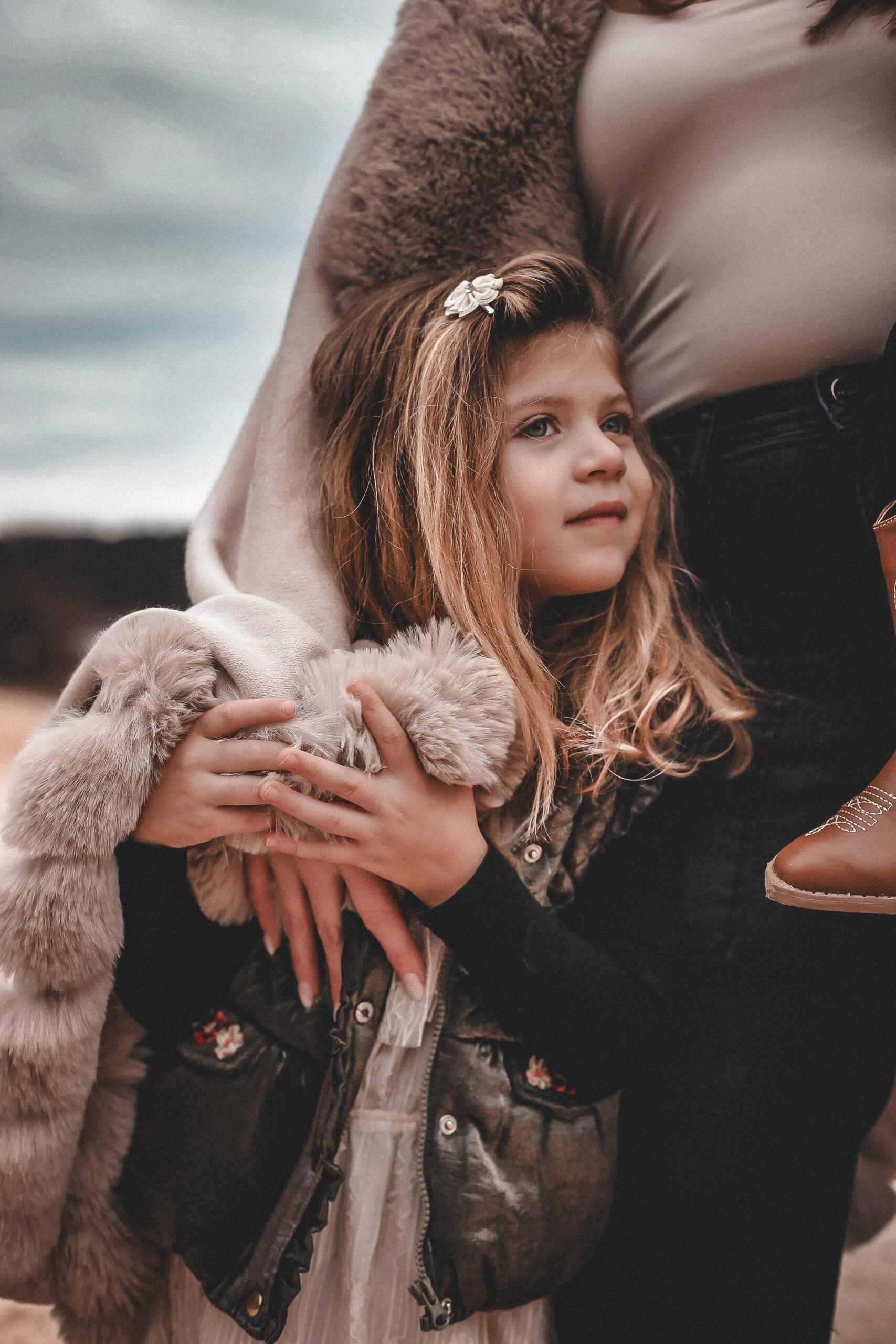 little girl at the beach holding her moms arm while look off into the distance