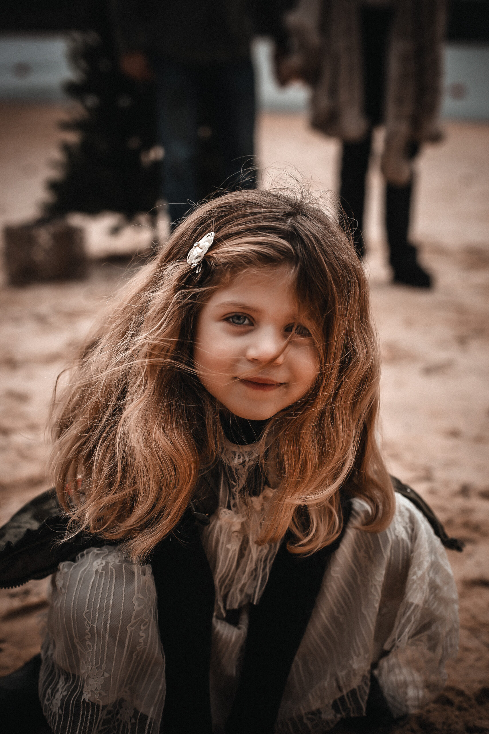 Close up portrait of a little girl on the sand with her hair blowing in the wind and looking at the camera while smiling softly