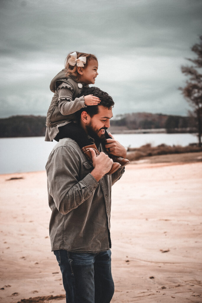 ortrait of little girl on her dads shoulders while laughing and at the beach