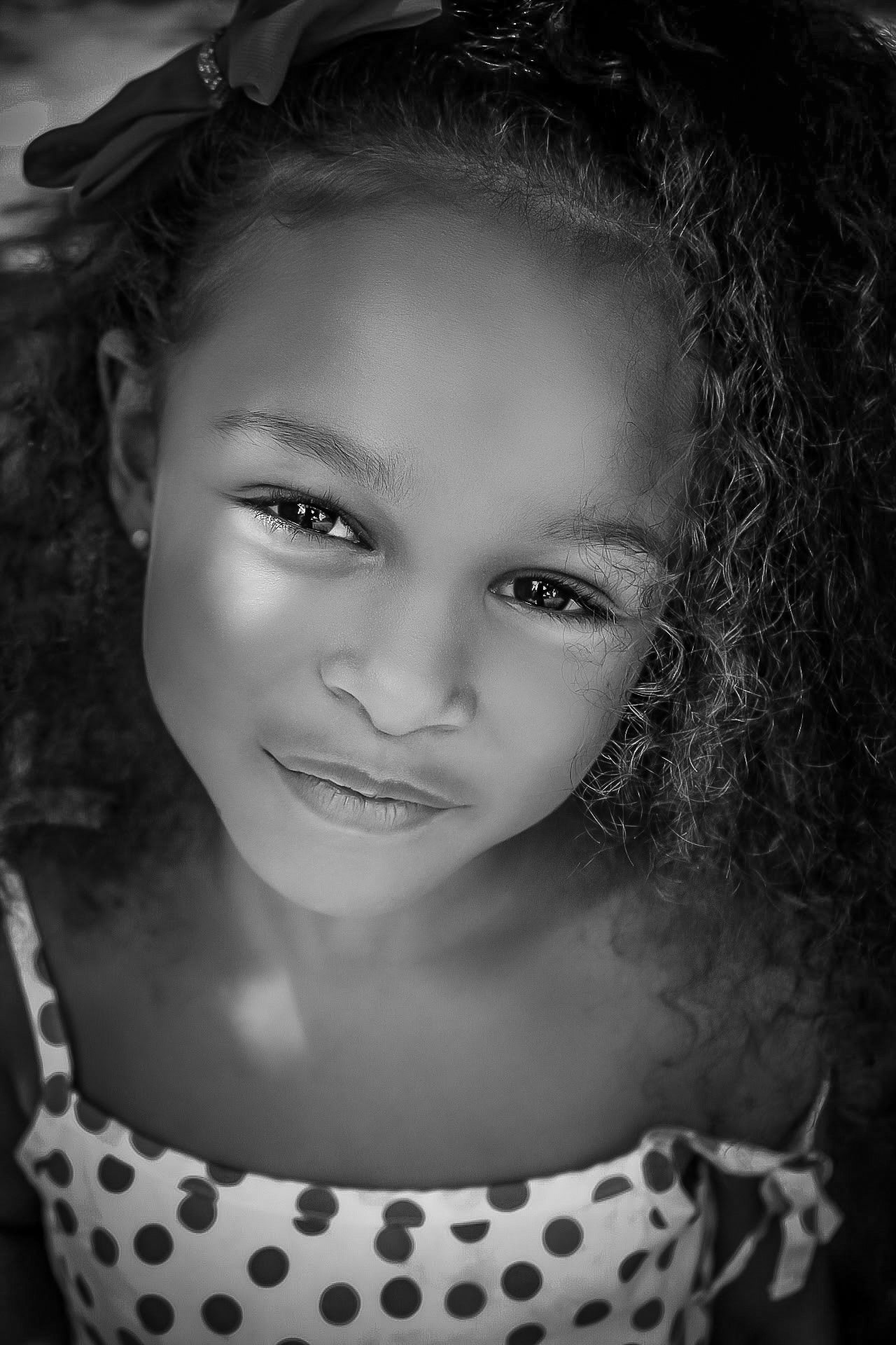 Black and white portrait of a little girl giving a soft smile at the camera during a hot summer day